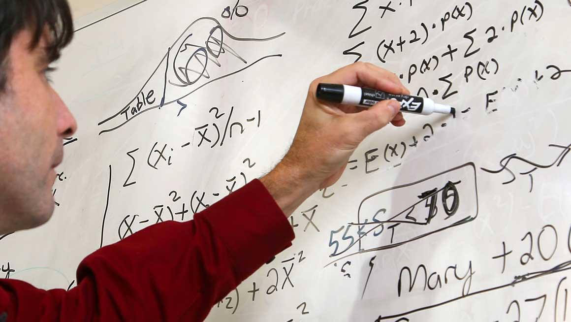 Professor James Bishop solves math equations on a whiteboard. 