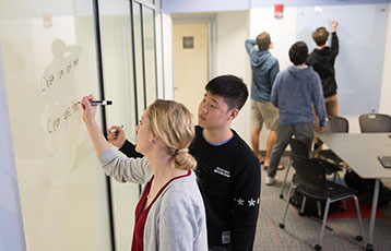 Bryant students in the College of Arts and Sciences write on a whiteboard