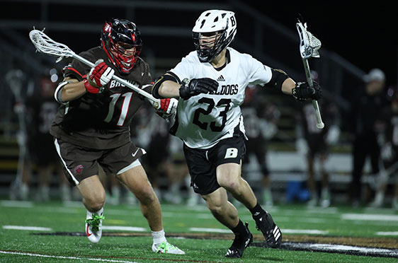 A Bryant University men's lacrosse player runs past a Brown University during a game at Beirne Stadium.