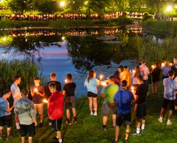 Dozens of students hold candles outside the pond.