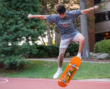 A student performs a trick on his skateboard on campus.