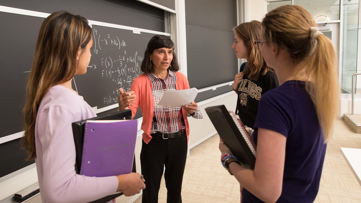 Bryant University Professor Karen Pitts talks with three students in front of a chalkboard.