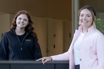 Two students pose for a photo at the welcome desk inside the Quinlan / Brown Academic Innovation Center at Bryant University.