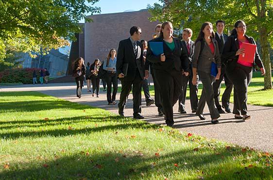 A group of students dressed in business attire walk along a stone path at Bryant University.