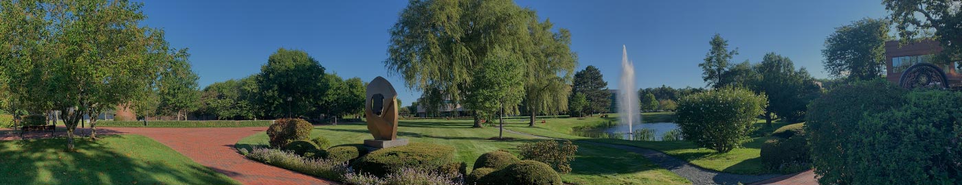 A golden sculpture in the center, surrounded by green trees and fields, with a lake and fountain in the background