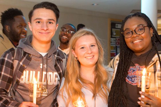 Three students hold up candles during Bryant University's Festival of Lights holiday celebration.