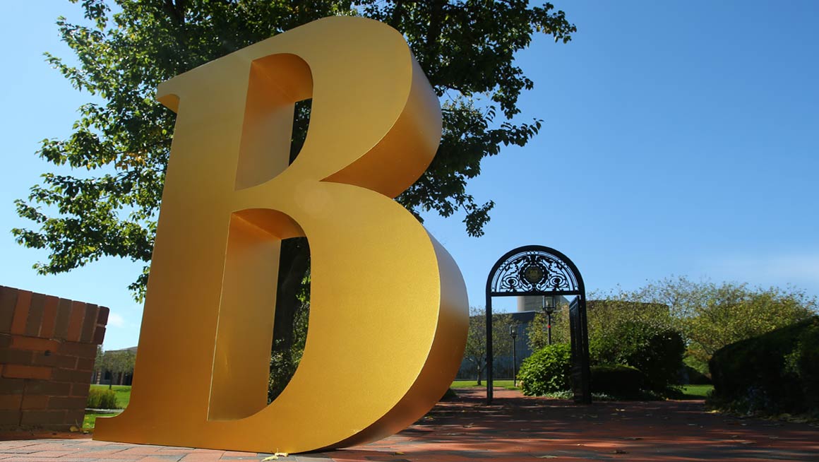 The letter "B" in the foreground on the brick walkway with the Bryant Archway in the background.