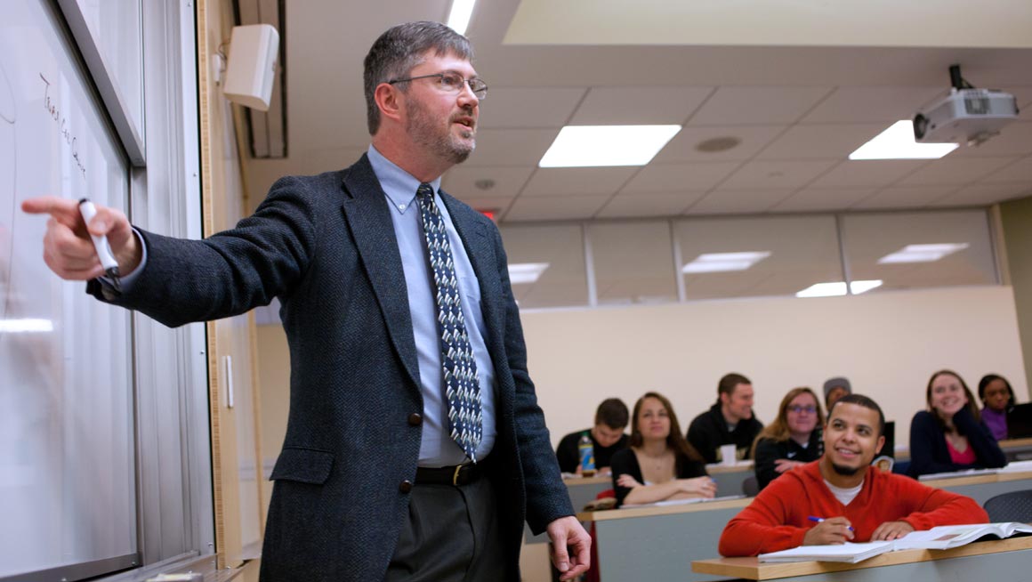 Bryant Professor Christopher Roethlein lectures to students in a classroom.