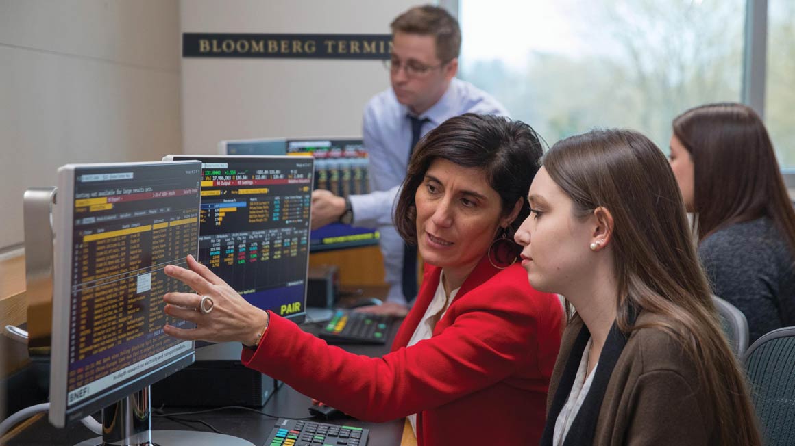 Bryant Professor N. Asli Ascioglu helps a student by the Bloomberg Terminals inside the George E. Bello Center for Information and Technology.