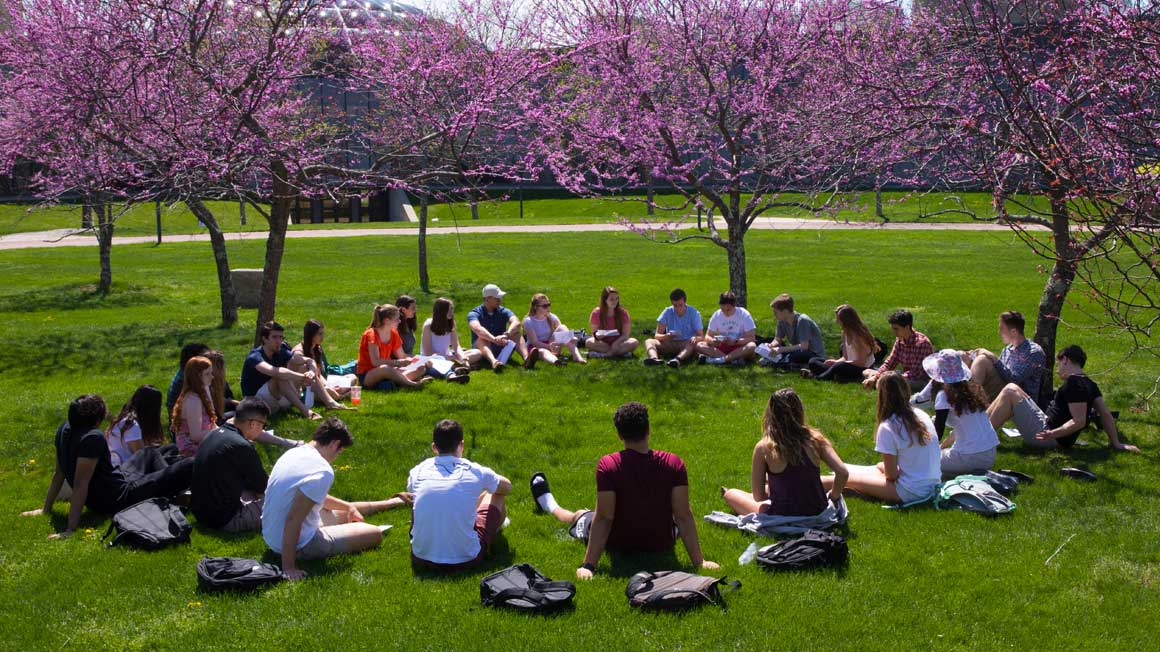 A group of students sit in a circle on the grass of the Bryant University quad
