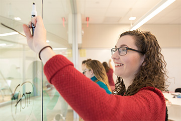 A student at Bryant University writes on the glass.