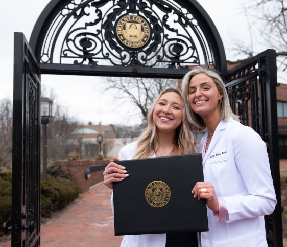 Class of 2023 graduates Anna McIntyre and Kelsey Heck pose by the Bryant archway.