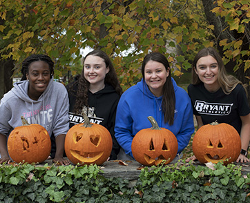 A group of four students stand behind the pumpkins they carved at Bryant University.