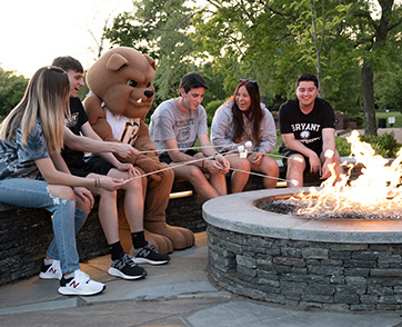 A group of students and the mascot make s'mores outside the Fisher Student Center.