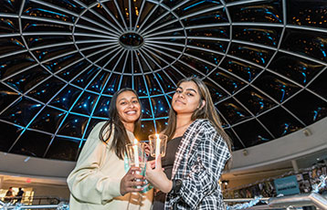 Two female students hold candles in the Rotunda during Festival of Lights, the holiday celebration at Bryant University.