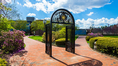 The Bryant University archway against a blue sky with clouds.