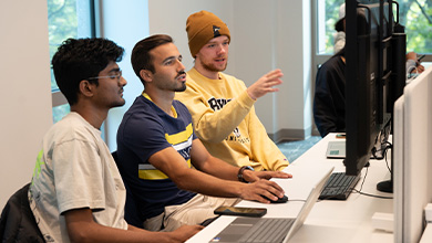 Three Bryant University students look at a computer monitor inside the Data Visualization Lab at Bryant University..