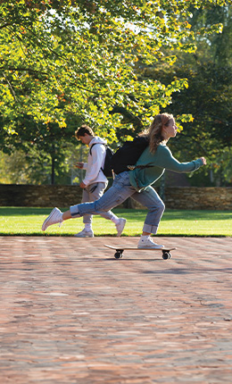 A Bryant student zooms across campus on a skateboard.